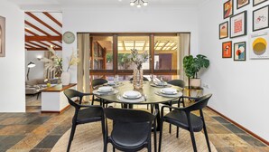 Comedor con una mesa redonda dispuesta para seis comensales, rodeada de sillas negras, con una araña colgante y un ventanal con cortinas.