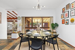 A dining area with a round table set for six, surrounded by black chairs, with a chandelier above and a large window with curtains. - Grand 3BR Heritage Home | Designer Living in North Perth (North Perth)