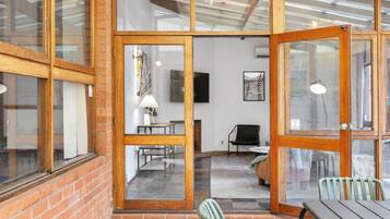 A room with a brick wall, wooden-framed glass doors, a flat-screen TV, a lamp, and a chair.