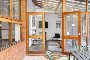 A room with a brick wall, wooden-framed glass doors, a flat-screen TV, a lamp, and a chair. - Grand 3BR Heritage Home | Designer Living in North Perth (North Perth)