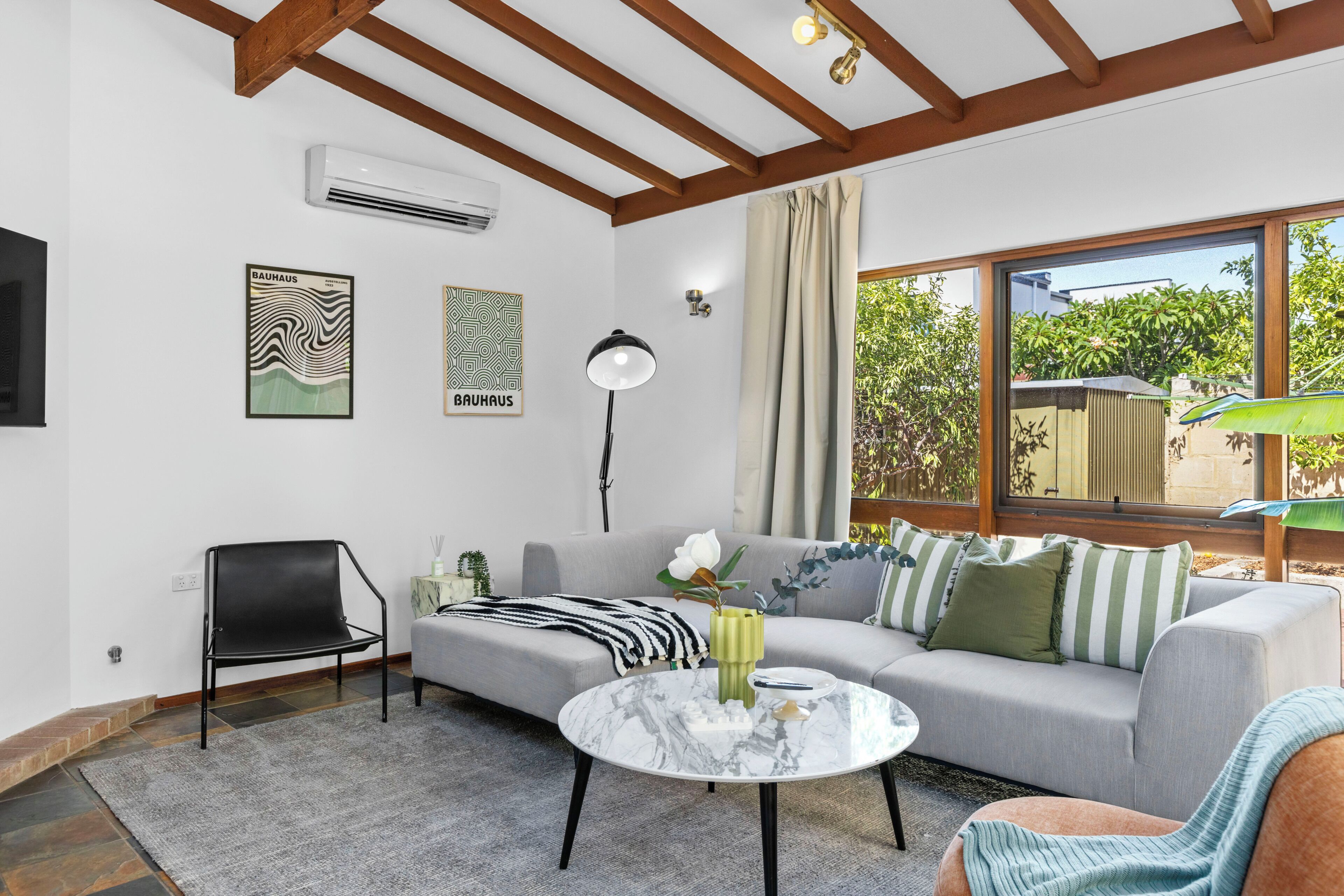 A modern living room with a sofa, a chair, a coffee table, and a large window with a view of greenery.