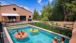 Une piscine avec des bouées gonflables, un patio couvert et un jardin aménagé.