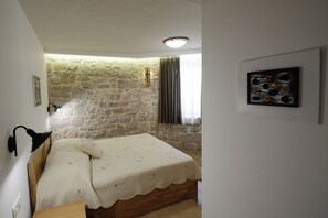 A bedroom with a stone wall, a bed with a white bedspread, a wooden headboard, a wall-mounted lamp, and a framed picture on the wall. - Apartment and Rooms Desideria (Split)
