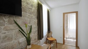 Une pièce avec un mur en pierre, un téléviseur à écran plat, une table à manger en bois, une chaise et une plante en pot.