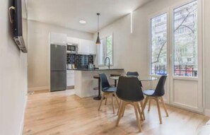 A modern kitchen with a refrigerator, microwave, and dining area with chairs. - Modern & Bright 3-Bedroom Apartment in Exclusive Salamanca District (Madrid)