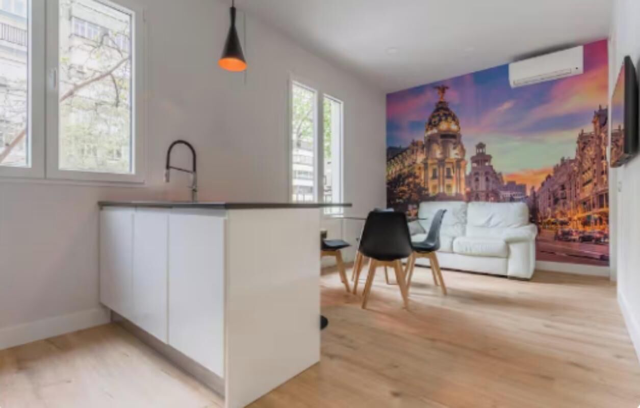 Een moderne keuken met witte kasten, een zwarte hanglamp en een eethoek met een witte bank en twee stoelen.