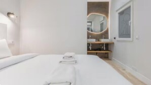 Ett hotellrum med en säng, ett sängbord, en spegel och ett badrum med handfat och handduksställ.