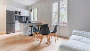 Ett modernt kök med matplats, stora fönster och en vit soffa.