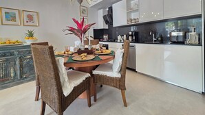 A modern kitchen with white cabinets, a dining area with wicker chairs, and a chandelier. - Anguila 102 – Stylish Beachfront Apartment Aqua Esmeralda, Dominicus (Dominicus)