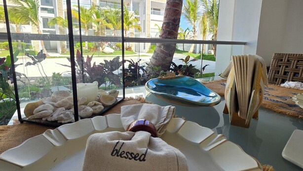 A room with a view of palm trees and a building, a table with towels, and a decorative fish. - Anguila 102 – Stylish Beachfront Apartment Aqua Esmeralda, Dominicus (Dominicus)
