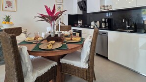 A modern kitchen with white cabinets, a dining table set with place settings, and a chandelier. - Anguila 102 – Stylish Beachfront Apartment Aqua Esmeralda, Dominicus (Dominicus)