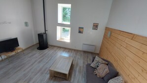 Una sala de estar moderna con televisor de pantalla plana, un calentador portátil, un banco de madera, un sofá con cojines estampados y una ventana con vistas a zonas verdes.