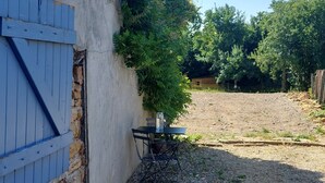 Un edificio con pared de piedra y un persiano azul, un camino de grava y una reja de metal.