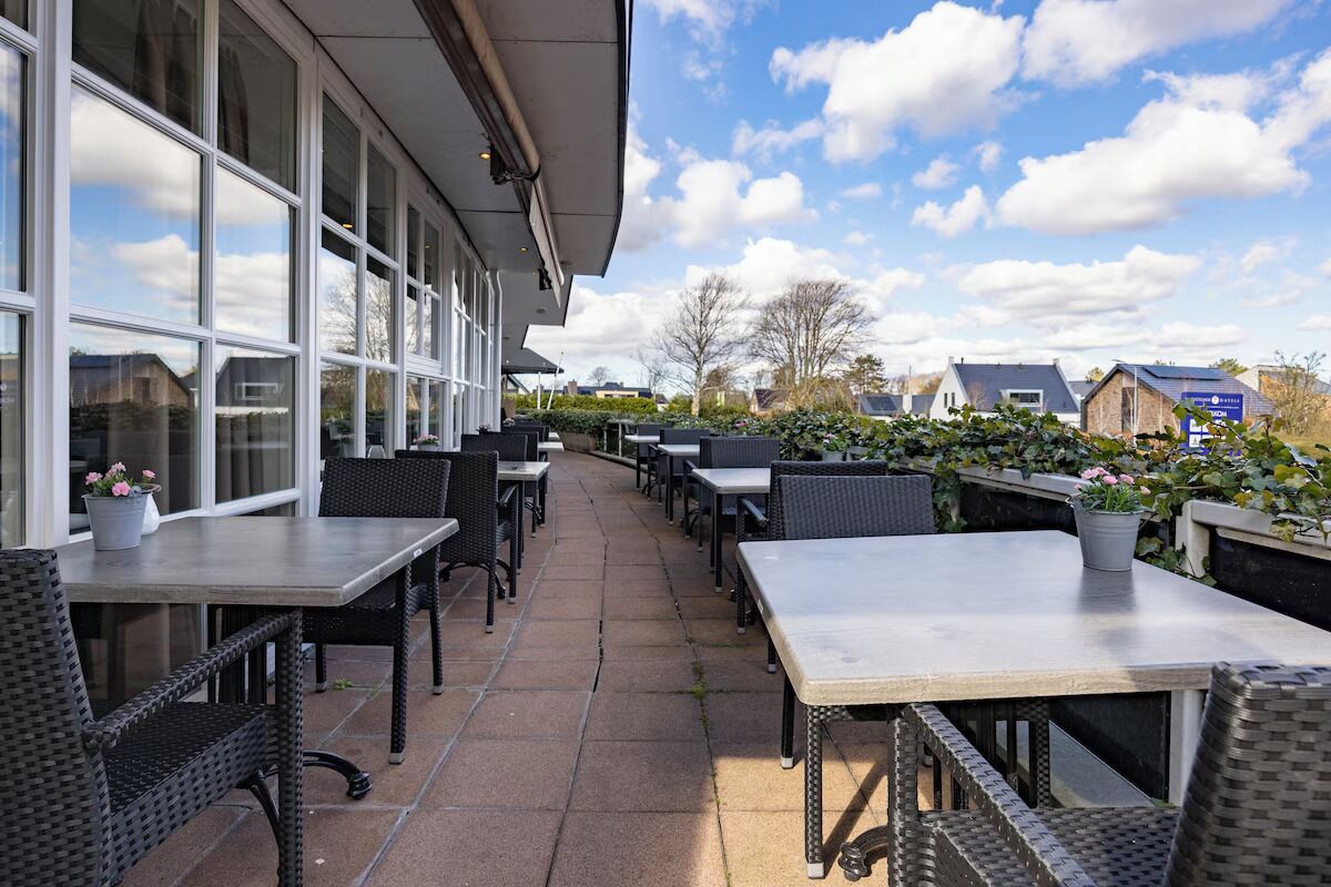 An outdoor patio area with tables and chairs, a building with large windows, and a clear sky.