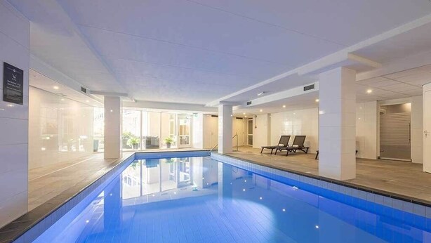 Ein Pool mit Fliesenboden, Liegestühlen und Blick ins Freie.