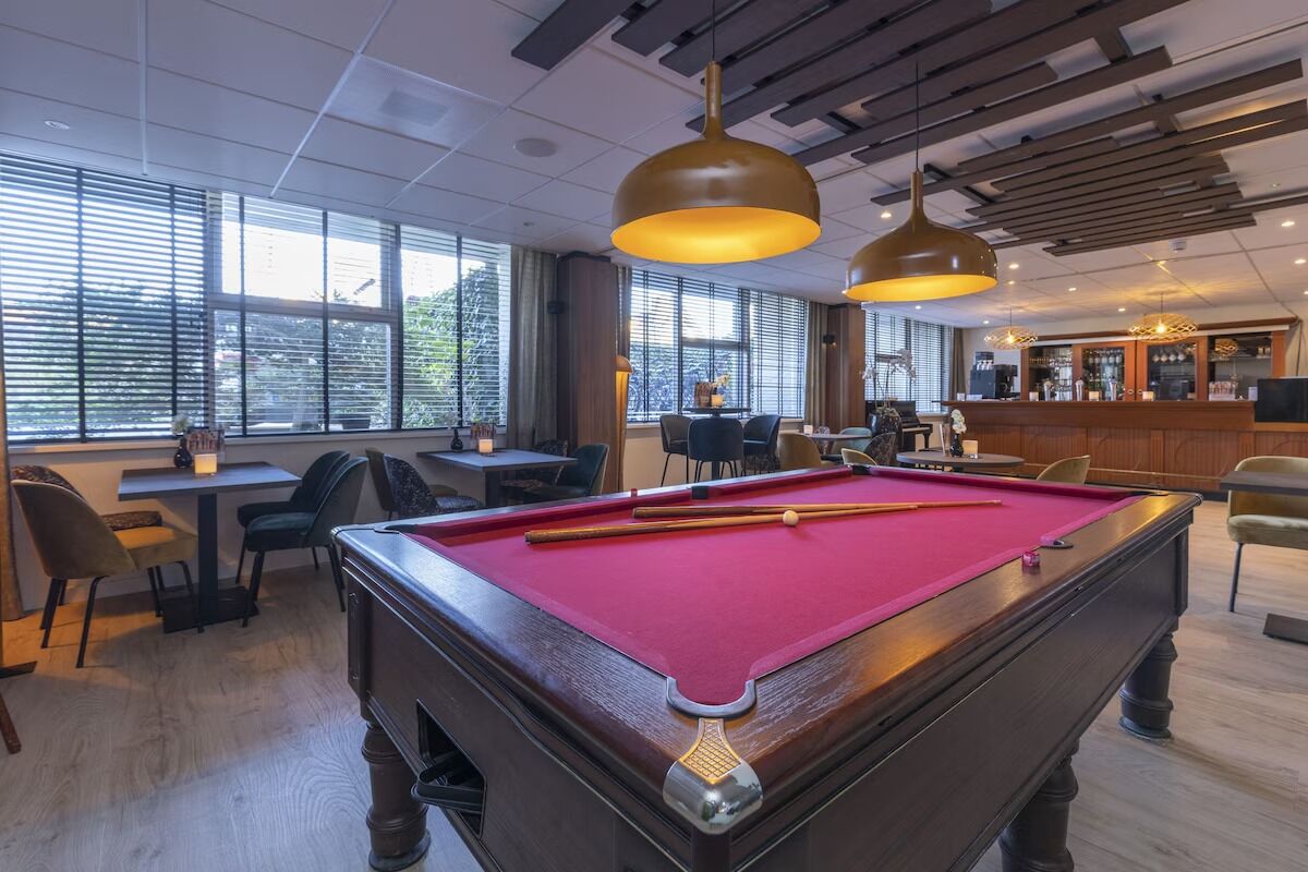 A pool table with a red felt surface, a bar area with a counter and stools, and a seating area with tables and chairs.