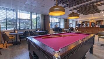 A pool table with a red felt surface, a bar area with a counter and stools, and a seating area with tables and chairs.