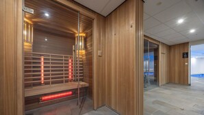 Ein modernes Interieur mit Holzverkleidung, einem Sauna-Bereich mit roter Beleuchtung und einem gefliesten Boden.