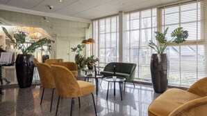 Eine Lobby mit einer Rezeption, gelben Sesseln, einem grünen Sofa und großen Kübelpflanzen.