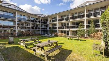 Un edificio de varios pisos, con mesas al aire libre y un patio cubierto de césped.