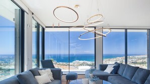 A modern living room with a large glass wall, a round glass coffee table, and a view of the coastline. - Lux 250m NEW Villa E with heated pool, ocean view (Costa Adeje)
