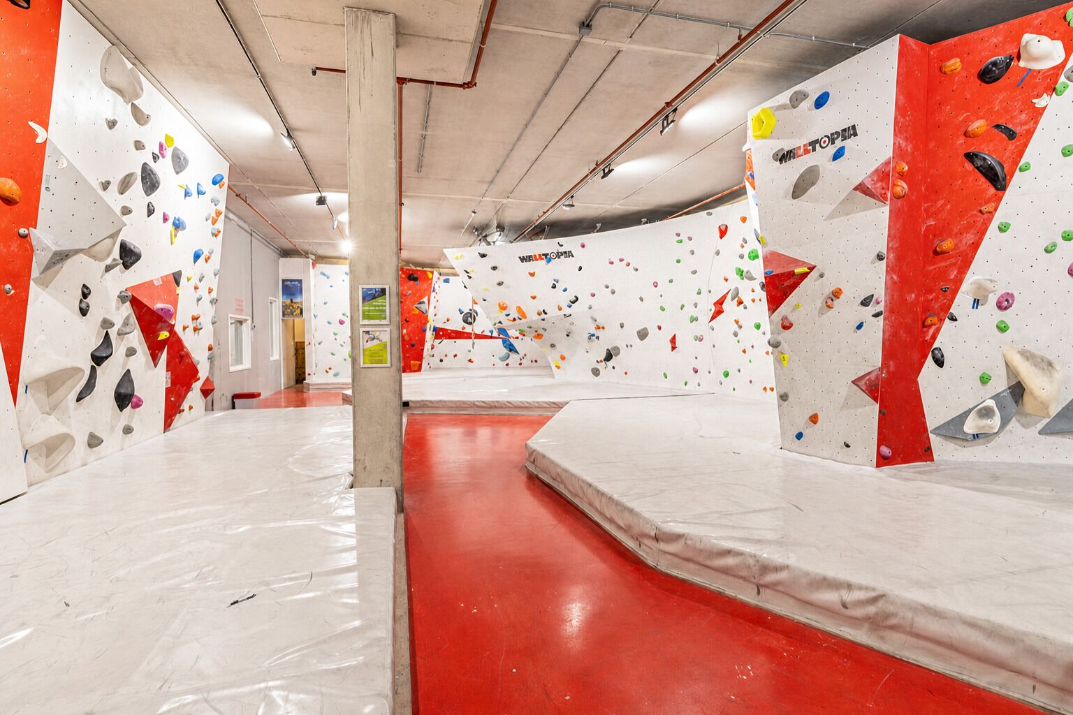 Une salle d’escalade intérieure dotée de plusieurs murs d’escalade, d’un sol rembourré et d’une allée centrale.