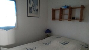 Een slaapkamer met een bed, een raam, een wandplank en een lamp.