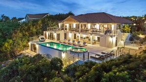 Une maison à deux étages avec une piscine, un espace salon extérieur et une terrasse couverte.