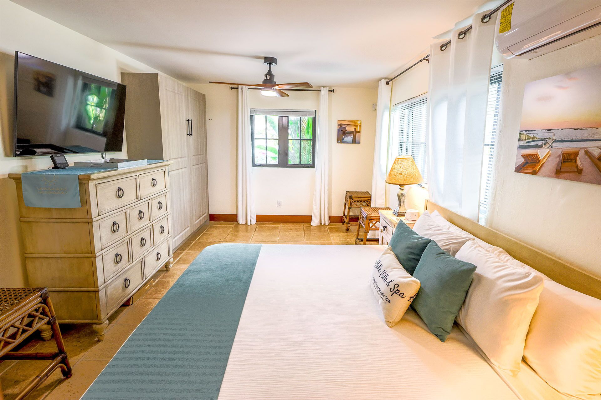 Un dormitorio con cama, televisor, escritorio y ventana con cortinas.
