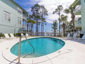 Una piscina con sillas de descanso, una escalera de piscina y vistas a un edificio con balcones y árboles.