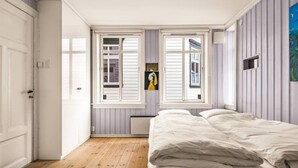 Un dormitorio con cama, dos ventanas, un radiador y una puerta.