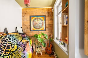 Una habitación con pared de madera, un tapiz colorido, una guitarra y una obra de arte grande enmarcada.