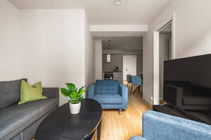 Un salon moderne avec un canapé gris, un fauteuil bleu, une table basse noire et une plante en pot.