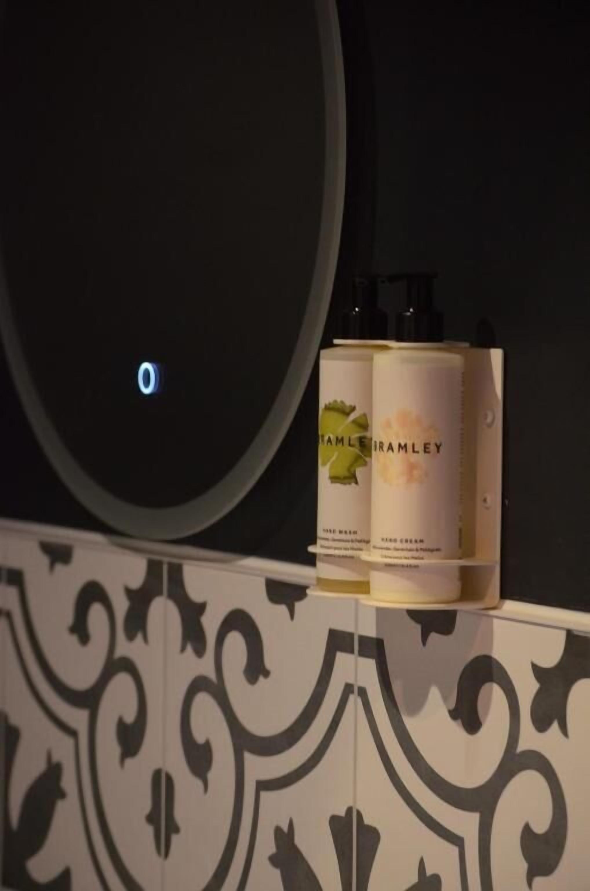 A bathroom with a mirror, a sink, and two bottles of Brambley hand cream on a shelf.