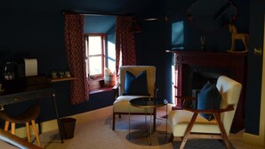 A room with a desk, two chairs, a round table, a fireplace, and a window with curtains.