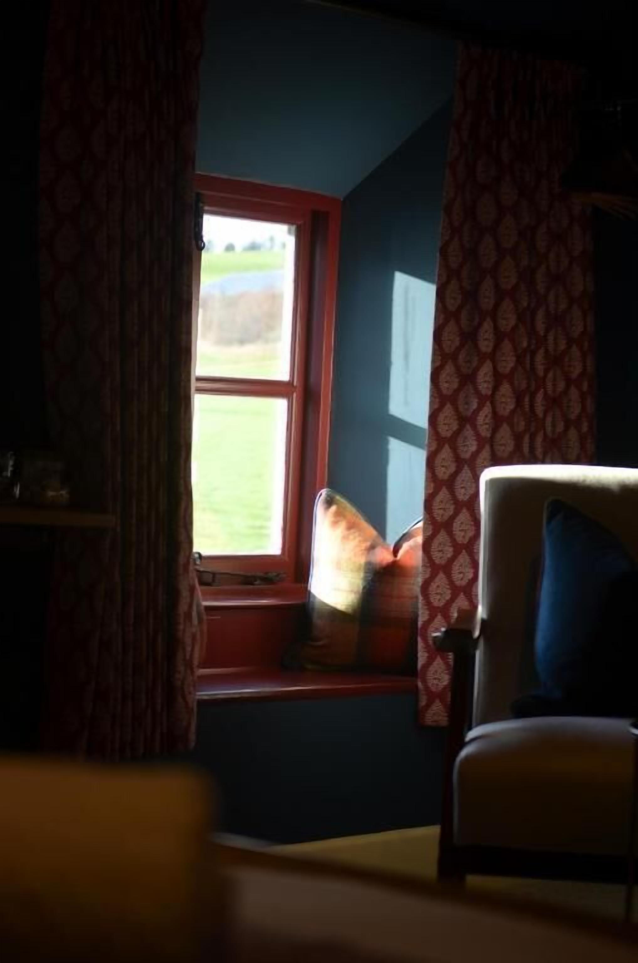 A room with a window, a chair, and a patterned curtain.