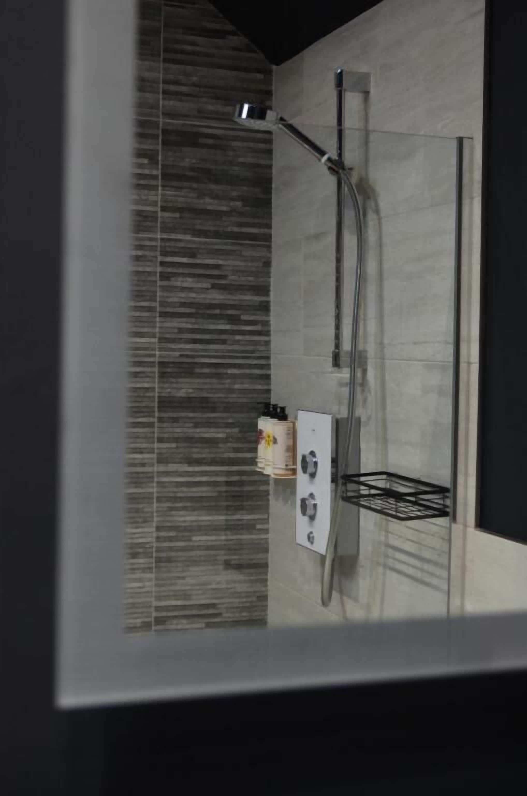Een moderne douche met een glazen douchecabine, bedieningspaneel en een metalen plank.