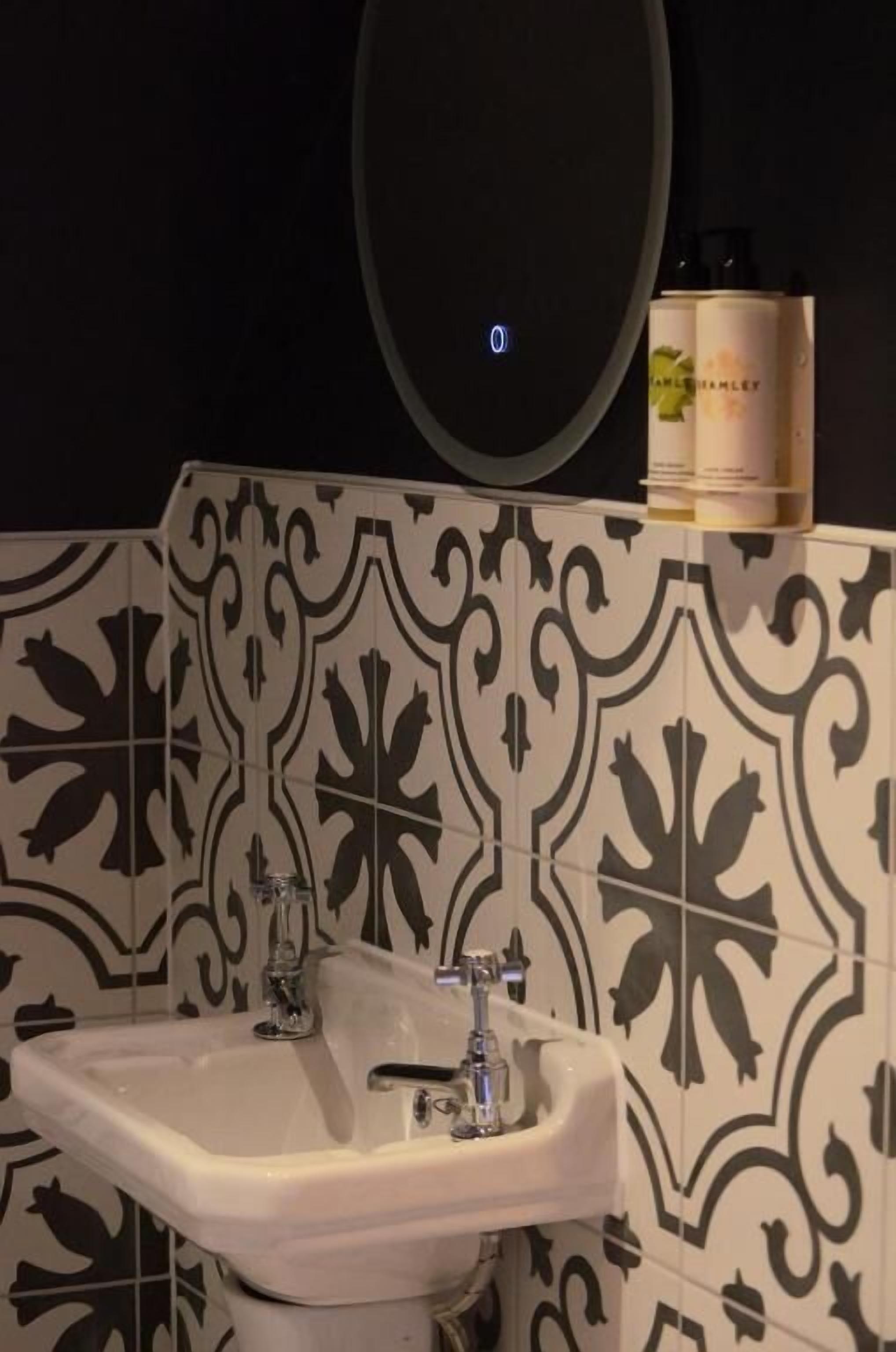 A bathroom with a white sink, black and white patterned tiles, and a mirror above the sink.