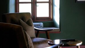 A room with a window, a chair, a small table, and a framed picture on the wall.
