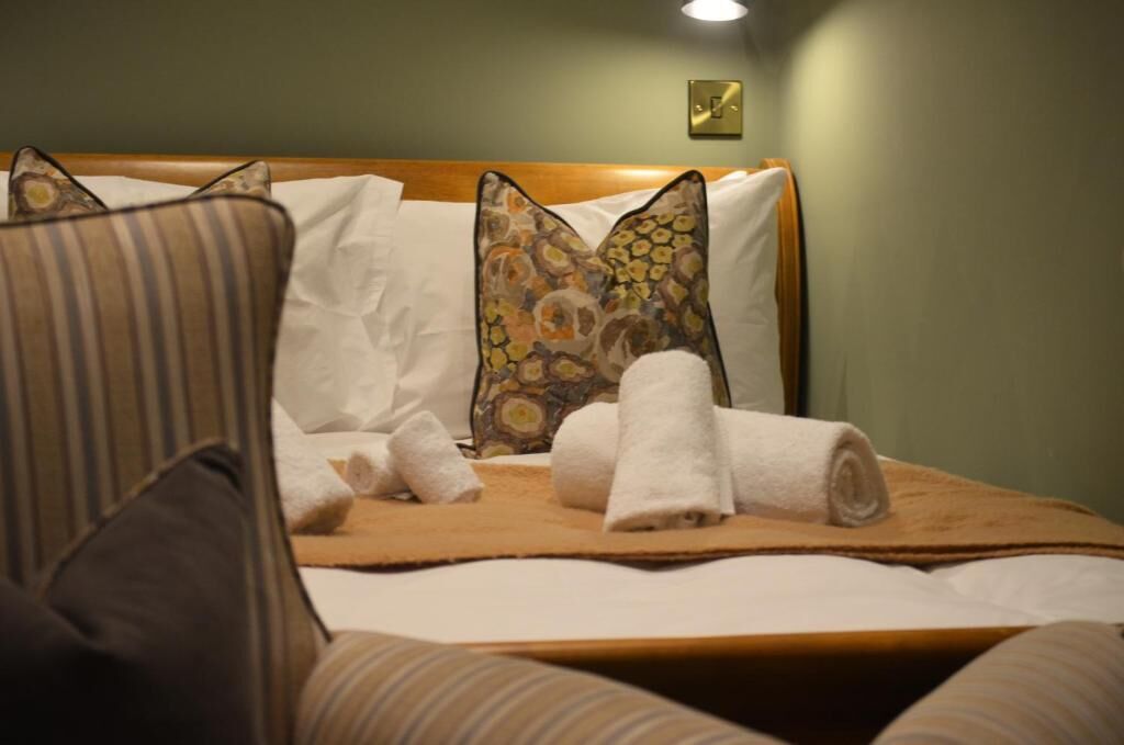 Una cama bien hecha con sábanas blancas, una almohada estampada y una toalla enrollada.