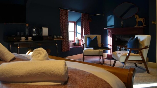 A cozy room with a bed, two chairs, a fireplace, and a window with curtains.
