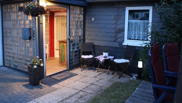 A house with a tiled roof, a front door, a small porch with two chairs, and a potted plant. - BergZeit Karles | Winterberg—Your Favorite Spot on the Rothaarsteig•Ski•Hiking•Bike Park (Winterberg)