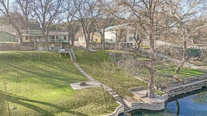 A residential area with a stone bridge over a pond, houses in the background, and a grassy lawn. - Guadalupe Riverfront Home | Decks, Firepit & Private River Access (Canyon Lake)
