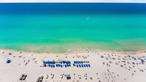 A beach with rows of umbrellas and sun loungers, a clear blue sea, and a sandy shore. - Gulf-Front Retreat | Stunning Views | Sleeps 6 | East PCB (Panama City Beach)
