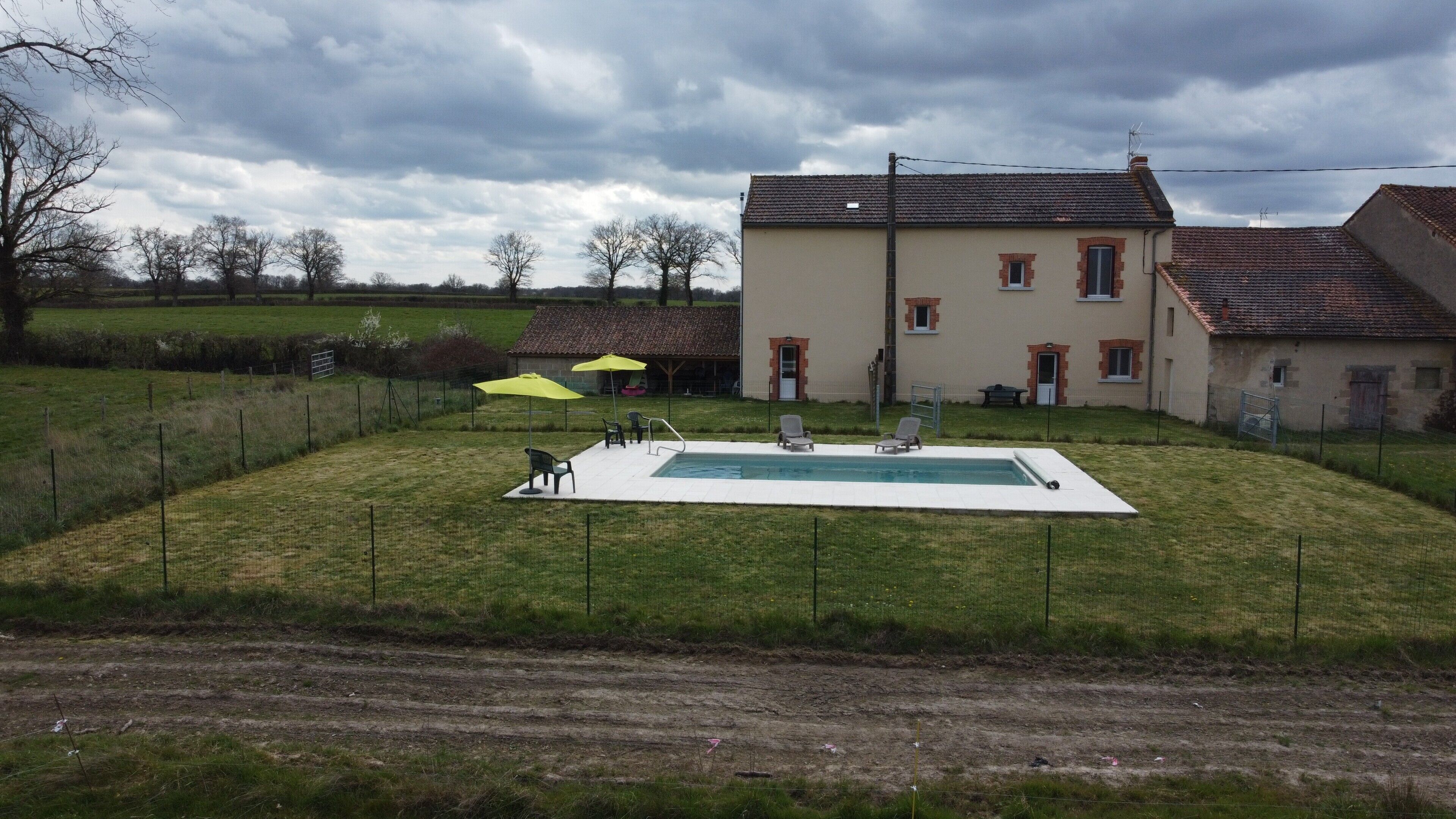 En boligejendom med swimmingpool, udendørs møbler og et stort hus med tegltag.
