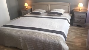 Een keurig opgemaakt bed met een wit-donker gestreepte deken, twee bedlampjes en een houten nachtkastje met lades.