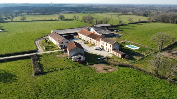 Luchtbeeld van een boerderij met meerdere gebouwen, een zwembad en omliggende groene velden.