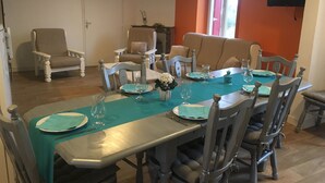 Een eetgedeelte met een tafel voor vier personen, omringd door stoelen, een klok aan de muur en een aan de muur bevestigde televisie.