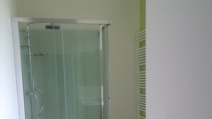 Een douche met glazen wanden, een wit douchebak, een houten vloer en een witte wastafel met een handdoekhouder.