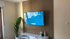 A modern living room with a mounted TV, a white entertainment unit, a potted plant, and a wooden panel wall.